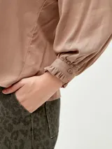 Blusa blanca de mangas largas con cuello fruncido y lazo.
