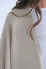Ruana color beige de tejido de punto con flecos en el ruedo.
