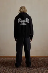 Campera negra con capucha, cierre frontal y bolsillos laterales. Estampado blanco con texto en el pecho.