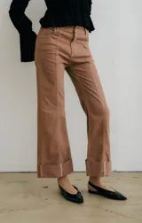 Pantalón de jean azul oscuro con corte acampanado, tiro medio y dobladillo en el ruedo. Presenta costuras marcadas en el frente y estampado abstracto en tonos grises y blancos en el interior del dobladillo.