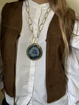 Collar con cadena de eslabones dorados y dije circular de bronce con piedra ágata en tonos celeste y azul.