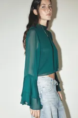 Camisa verde esmeralda de cuello alto y manga larga con volantes en los puños. Cierre en la espalda con abertura y botones.
