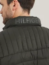 Campera acolchada verde militar de Tommy Hilfiger, con cuello alto, cierre de cremallera, dos bolsillos delanteros con cremallera y logo de Tommy Hilfiger bordado en el pecho.