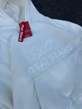 Buzo hoodie color crema con bolsillo tipo canguro y logo de la marca bordado en el frente.