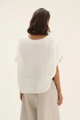 Blusa blanca con rayas verticales grises, corte holgado, mangas cortas con detalle desflecado y cuello redondo.