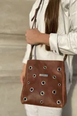 Bandolera marrón de cuero con apliques metálicos y correa fina regulable.