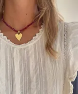 Collar corto confeccionado con una hilera de cuentas facetadas en color bordó y un dije central en forma de corazón dorado con acabado liso.