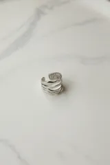 Anillo plateado ajustable de acero quirúrgico hipoalergénico, con diseño de líneas onduladas.
