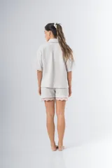 Conjunto de pijama de tela waffle color crema, compuesto por una camisa de manga corta con botones, bolsillo y detalle de broderie, y un short con elástico y cordón en la cintura con terminación de broderie.