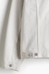 Campera de denim color crudo, de corte recto, con cuello clásico, cierre frontal con botones metálicos, bolsillos con solapa en el pecho y bolsillos laterales.