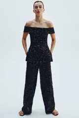 Pantalón negro de tiro alto con lentejuelas, corte palazzo y cierre frontal con cremallera, botón interior y gancho metálico.