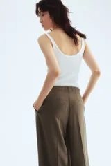 Pantalón tobillero color verde oliva de corte holgado, tiro alto, con elástico oculto en la cintura, cierre con botón, bolsillos al bies y bolsillos decorativos atrás. Presenta pliegues de tabla adelante, pinzas en la parte posterior y piernas amplias con raya adelante y atrás.