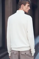 Polera blanca de punto fino, con cuello alto, mangas largas y corte ajustado.