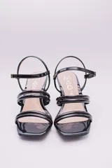 Sandalias de ecocuero charolado color negro, con punta cuadrada, dos tiras horizontales sobre el empeine, pulsera con hebilla al tobillo y taco cuadrado.