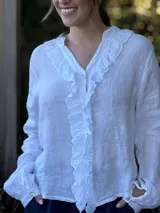 Camisa blanca de lino con cuello mao, mangas largas abullonadas y cierre frontal con botones de nácar. Presenta volados en el frente y puños elásticos.