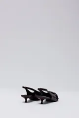 Zapato de tacón bajo tipo slingback, color bordó oscuro con acabado charol. Presenta punta fina y una tira decorativa con hebilla metálica en el empeine, además de una tira ajustable con hebilla en el talón.
