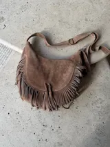 Cartera bandolera marrón de gamuza con flecos en el frente y correa ajustable.
