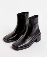 Bota corta de cuero charol negro, con caña baja, cierre lateral y taco cuadrado de madera.