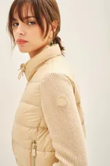 Campera color beige con mangas tejidas, cuello alto y cierre frontal.
