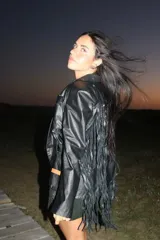 Chaqueta de cuero negra con solapas, cierre frontal con broche y flecos en mangas y ruedo.