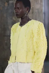 Chaqueta corta color amarillo pastel con textura de volantes, cuello redondo, manga larga y cierre frontal con botón a presión oculto.