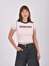 Remera corta de color rosa claro con cuello redondo negro, mangas cortas y estampado con texto y damero de carreras.