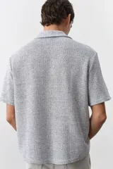 Camisa de manga corta color gris claro, de punto con textura de mezcla de algodón. Modelo con cuello abierto, tapeta lisa y bajo recto. Corte estándar para una silueta clásica y cómoda.