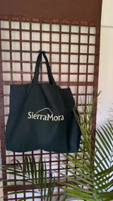 Bolso tipo tote bag de tela color verde oscuro con asas negras y logo Sierra Mora estampado en blanco.
