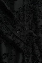 Camisa negra con textura, cuello de pico, botones delanteros, canesú con pliegues en la espalda, mangas largas con hombros caídos, puños abotonados y bajo redondeado.