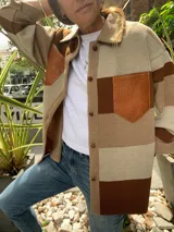 Camisa marrón con bloques de color beige y marrón oscuro. Presenta cuello camisero, cierre frontal con botones y un bolsillo de cuero en el pecho.