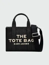 Bolso tote pequeño Marc Jacobs, tejido en color negro, con manijas cortas y correa larga ajustable. Estampado frontal con el texto "THE TOTE BAG MARC JACOBS" en color blanco.