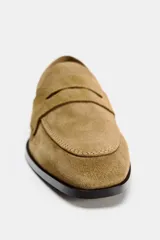Zapato plano tipo mocasín color marrón claro, confeccionado en piel de serraje. Tiene copete subido, antifaz y punta redonda.