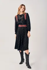 Vestido negro con estampado de hojas, corte midi, mangas largas abullonadas y cuello redondo. Presenta detalles bordados en rojo, blanco y azul en los hombros y la cintura.