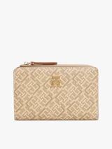 Billetera plegable color beige con estampado del logo de Tommy Hilfiger en toda la superficie. Tiene cierre de cremallera, múltiples ranuras para tarjetas, compartimento para billetes y bolsillo exterior para monedas.
