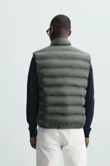 Chaleco acolchado color verde oscuro, con cuello alto y cierre frontal con cremallera.