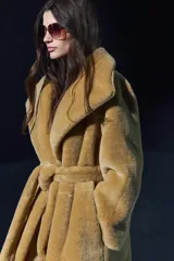 Abrigo largo color camel con efecto piel de oveja, cuello solapa, manga larga, bolsillos delanteros y cinturón ajustable con lazadas. Forro interior.