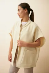 Chaleco color crema de lana sin teñir, corte recto, con cuello y solapa pronunciadas, broches a presión y bolsillos ojal.