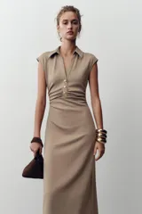 Vestido midi color beige con cuello polo, escote en pico, manga sisa caída y detalle de drapeado lateral. Cierre frontal con botones metálicos en relieve.