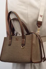 Bolso tipo shopper color marrón con doble asa corta y correa larga extraíble. Tiene detalle de pespuntes y anilla metálica decorativa. Incluye bolsa de tela interior extraíble con cierre fruncido.