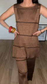 Top marrón de tejido de punto con textura acanalada, corte recto, sin mangas y cuello redondo. Presenta terminaciones en pico y botones decorativos con forma de flor.