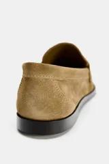 Zapato plano tipo mocasín color marrón claro, confeccionado en piel de serraje. Tiene copete subido, antifaz y punta redonda.