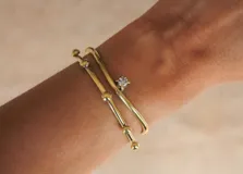 Pulsera rígida de bronce dorado con diseño minimalista y una zirconia engarzada.