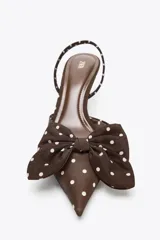Zapato de tacón marrón con estampado de lunares blancos, tira trasera con elástico, punta fina y detalle de lazo en la parte delantera.
