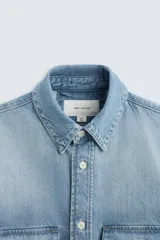 Camisa celeste de denim de algodón, corte relaxed fit, con cuello solapa, manga larga con puños abotonados, dos bolsillos de parche con solapa en el pecho, efecto lavado y cierre frontal abotonado.