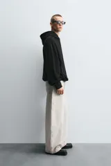 Sudadera negra de tejido con textura acanalada, corte boxy, capucha con cordón ajustable, manga larga con puños acanalados y bajo con elástico.