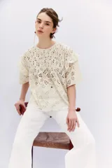 Blusa blanca de broderie con escote redondo, mangas cortas con volados en sisa y detalle de alforzas en el canesú.