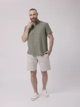 Camisa de hombre color verde oliva, de manga corta y corte clásico. Confeccionada en lino y poliéster, con cuello abotonado y bolsillo en el pecho.