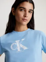 Remera cropped de color celeste, confeccionada en algodón regenerativo, con cuello redondo y manga corta, estampada con monograma 3D de Calvin Klein.