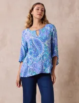 Blusa de gasa estampada con motivos paisley en tonos azules, marca Ruby Rd. Tiene cuello redondo con escote en V y aplique metálico. Presenta una sobre capa delantera y terminación asimétrica. Las mangas son 3/4 y amplias.