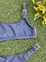 Conjunto de bikini azul con corpiño de breteles finos y hebillas metálicas en los tirantes. La bombacha es colaless y también tiene hebillas metálicas en los laterales.